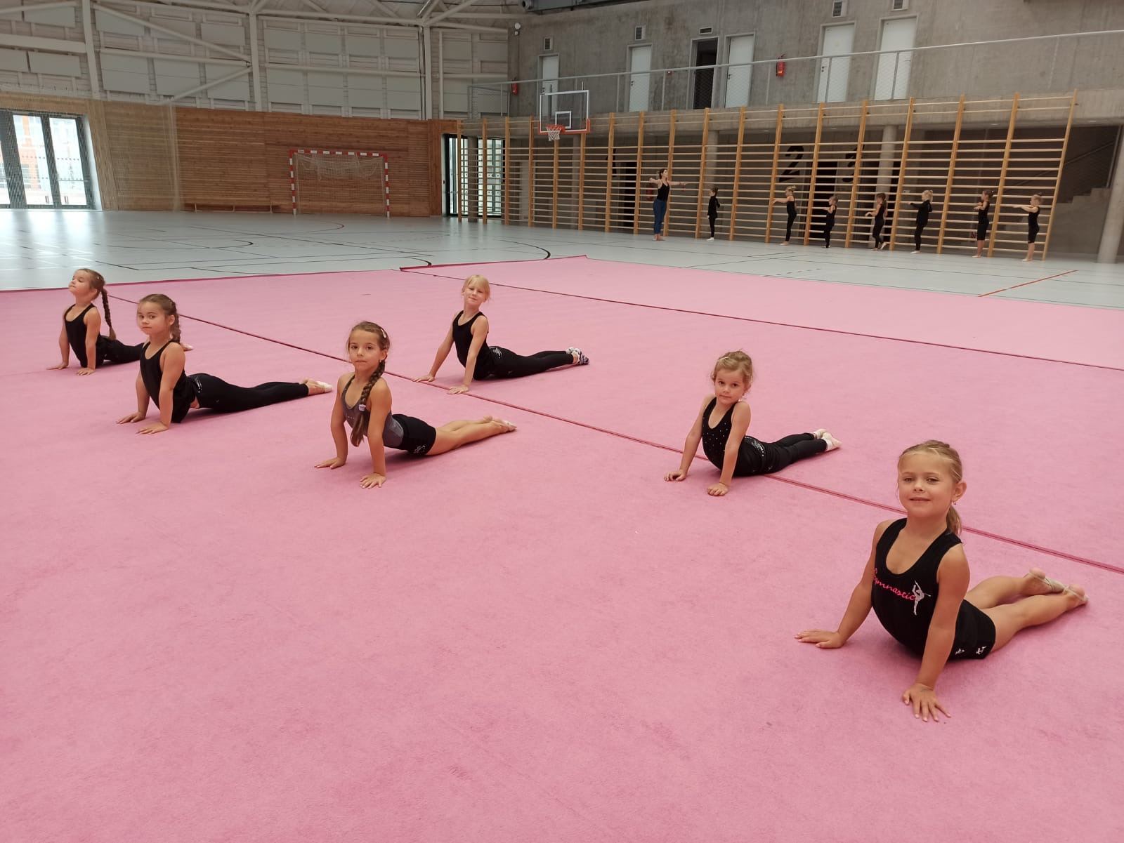 Gymnastky z kroužku se protahují na růžovém koberci