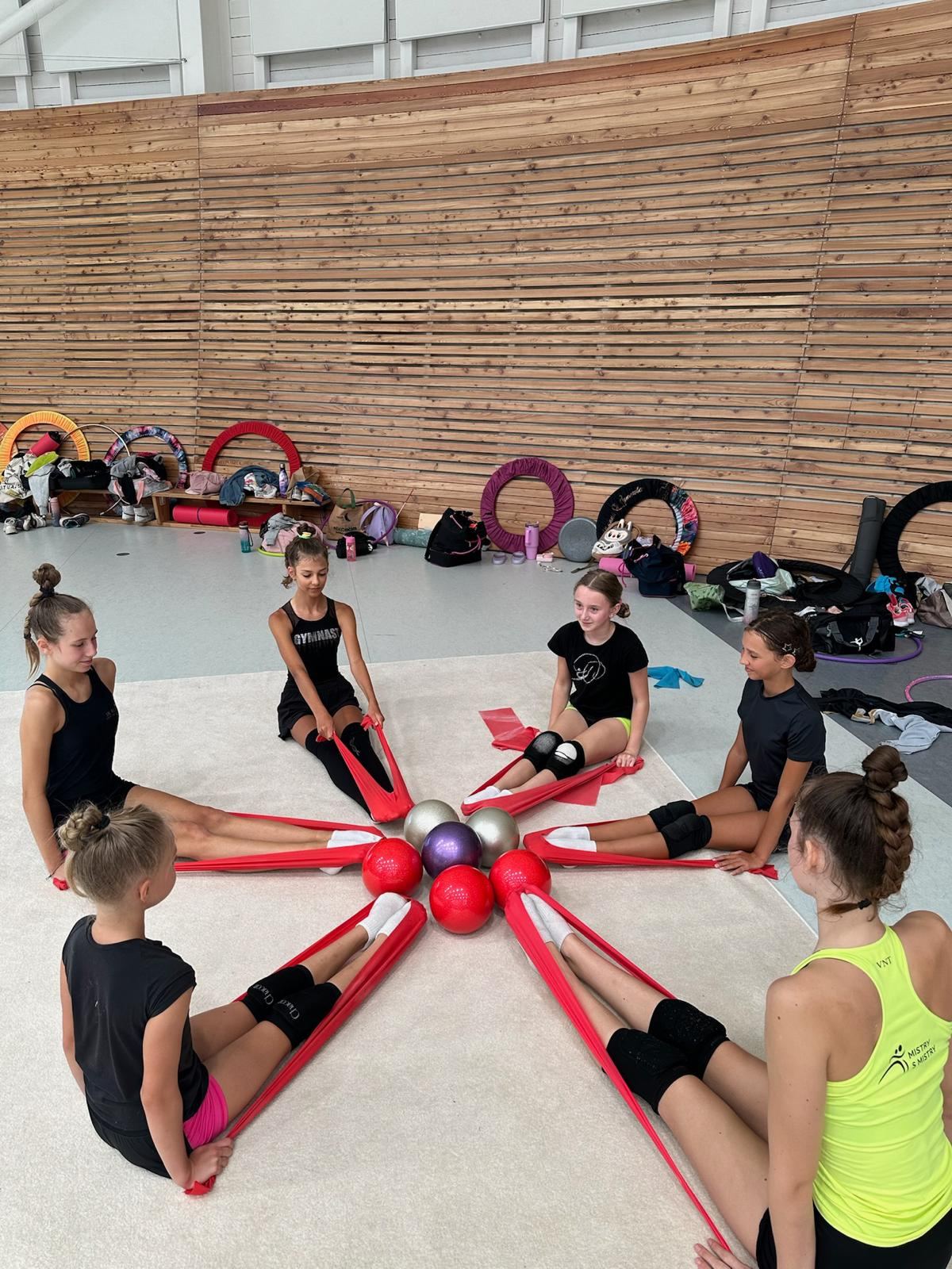 Družstvo gymnastek sedí v kruhu se stuhami a míči
